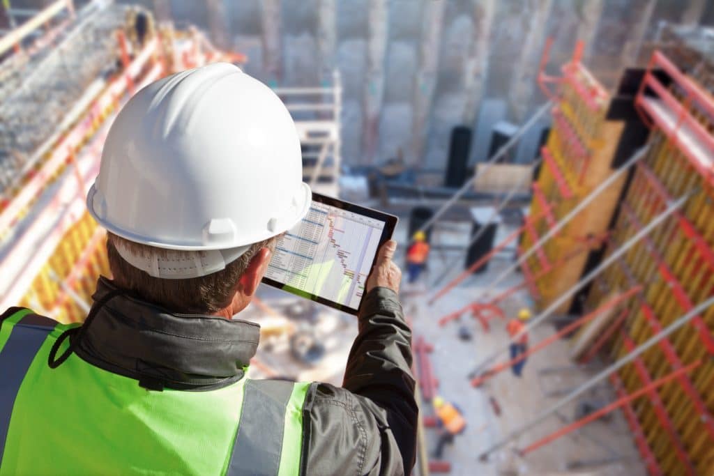 An engineer with a tablet looks down on a multi-level commercial construction site.
