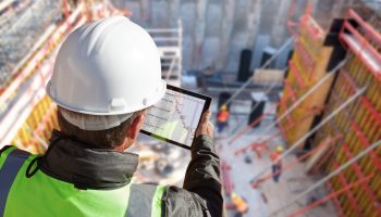 An Engineer With A Tablet Looks Down On A Multi-level Commercial Construction Site.