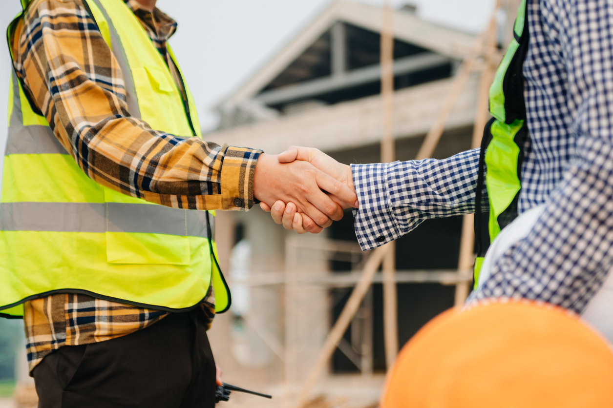 Two men in safety vests shaking hands at a commercial construction site.