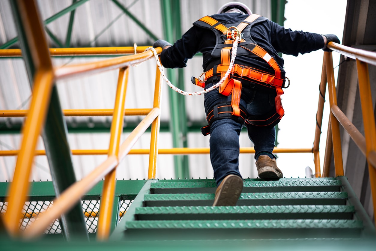 A construction worker climbing stairs while wearing a safety harness locked to the nearby railing.